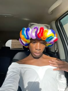 a woman in a white top and colorful hair is sitting in the back seat of a car