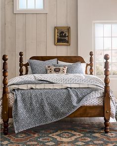 a bed with wooden posts and pillows on top of it in a bedroom next to a window