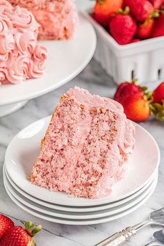 two slices of strawberry cake on plates with strawberries in the background