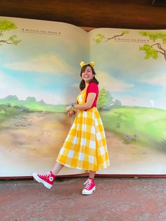 a girl in a yellow and white checkered dress is standing next to an open book