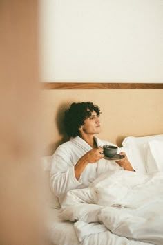 a man laying in bed holding a cup of coffee and looking up at the sky