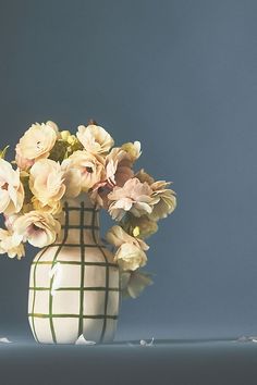 a white vase filled with lots of flowers on top of a blue table next to a wall