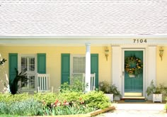 a yellow house with green shutters and potted plants on the front porch area