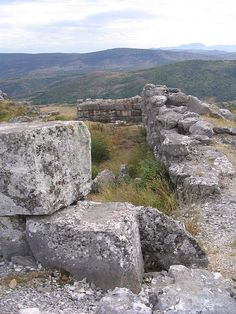 some rocks and grass on top of a hill with mountains in the distance behind them