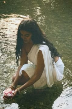 a woman sitting in the water holding a flower