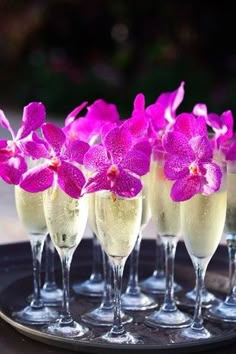 four glasses filled with champagne and pink flowers on a tray next to some wine glasses