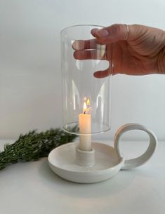 a person holding a lit candle in front of a glass cup on a white table