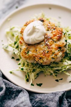 a white plate topped with crab cakes and lettuce covered in sour cream sauce