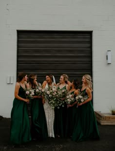 a group of women standing next to each other in front of a garage door holding bouquets