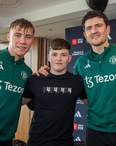 three young men standing next to each other in front of a wall with a soccer ball on it