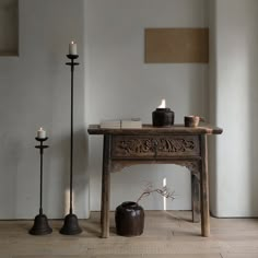 an old table with candles on it next to two black candle holders and a vase