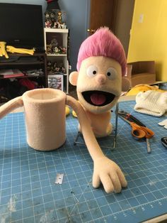 a cartoon character sitting on top of a table next to a cup with pink hair