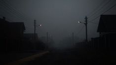 a dark street with power lines on both sides and houses in the distance at night