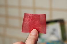 a hand holding a piece of red material in front of a tiled wall and floor