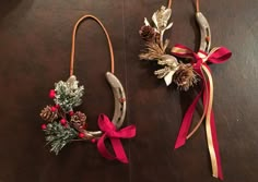 two christmas wreaths hanging from hooks on a wooden table with ribbons and pine cones