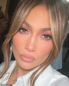 a close up of a person wearing a white shirt and gold necklace with pink eyeshadow