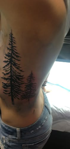 the back of a woman's stomach with pine trees on her lower side tattoo