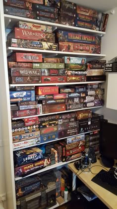 a computer desk topped with lots of video game boxes on top of a book shelf