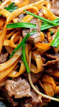 stir fried noodles with beef and green onions on a black plate, ready to be eaten