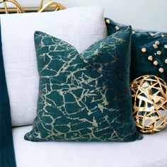 two decorative pillows on a white couch with blue and gold accessories in the back ground