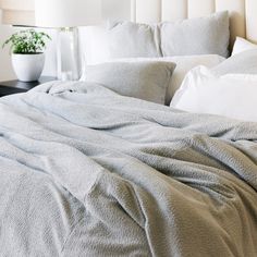 an unmade bed with white pillows and blankets on top of it, next to a potted plant