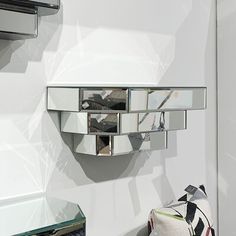 a mirror mounted to the side of a white wall next to a small table with a pillow on it