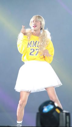 a female in a yellow shirt and white skirt on stage with her hands out to the side