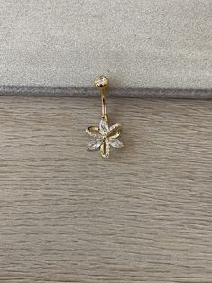 a gold and white diamond dragonfly belly button ring on a wooden surface with a gray background