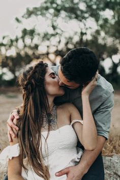 a man and woman kissing while sitting on a rock