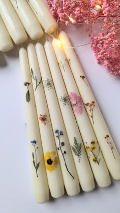 white candles with flowers painted on them sitting next to pink and yellow flowers in the background