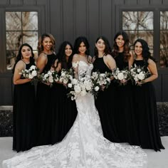 a group of women standing next to each other in front of a black wall holding bouquets