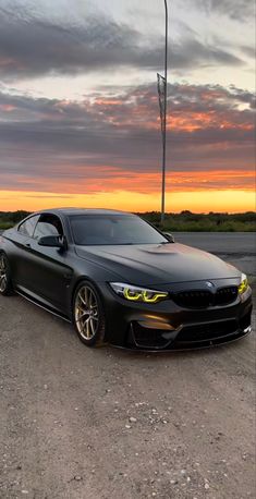 a black car parked on top of a parking lot next to a street light at sunset