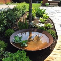 a large metal bowl filled with water surrounded by plants and trees on a wooden walkway