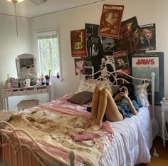 a woman laying on her bed reading a book in the middle of a room with posters all over it