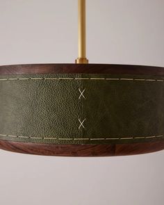 a green leather lamp shade hanging from a wooden ceiling fixture with gold stitching on it