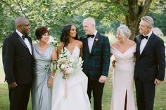 a group of people standing next to each other in front of a tree and grass field