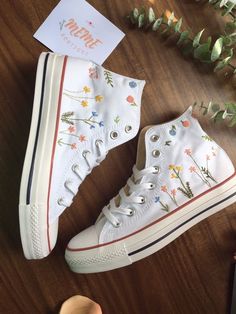 a pair of white high top sneakers with flowers on them sitting on a wooden table