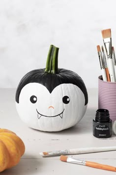 a painted pumpkin with a face on it next to paintbrushes and other items