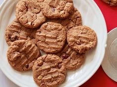 a white plate topped with chocolate chip cookies next to a pile of pennets on a red table cloth