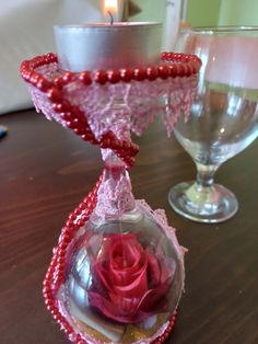 two wine glasses on a table, one with a rose in it and the other with beads