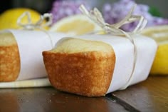 two muffins wrapped in white paper on a wooden table with lemons behind them