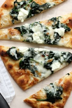 four slices of pizza with spinach and cheese on them sitting on a paper towel