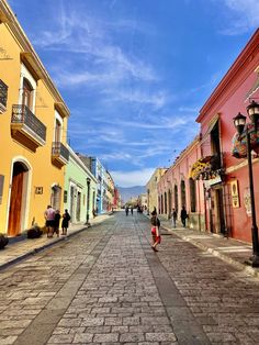 people are walking down an empty street with colorful buildings on either side and blue sky in the background