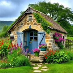 a small stone cottage with flowers and plants around the front door is surrounded by greenery