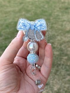 a hand holding a blue and white bow brooch with pearls on it's end