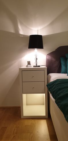 a white night stand next to a bed in a room with hardwood floors and walls