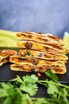 several quesadillas stacked on top of each other next to cilantro