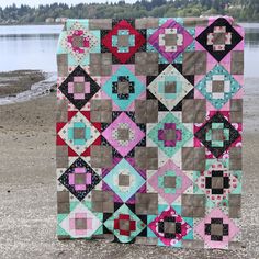 a patchwork quilt sitting on top of a sandy beach next to the water's edge