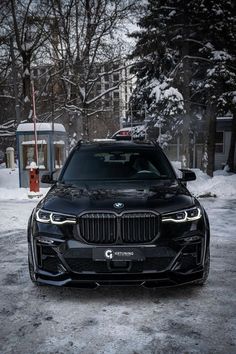 the front end of a black bmw suv parked on snow covered ground next to trees