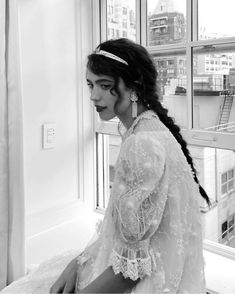 a woman sitting on top of a bed in front of a window with long hair